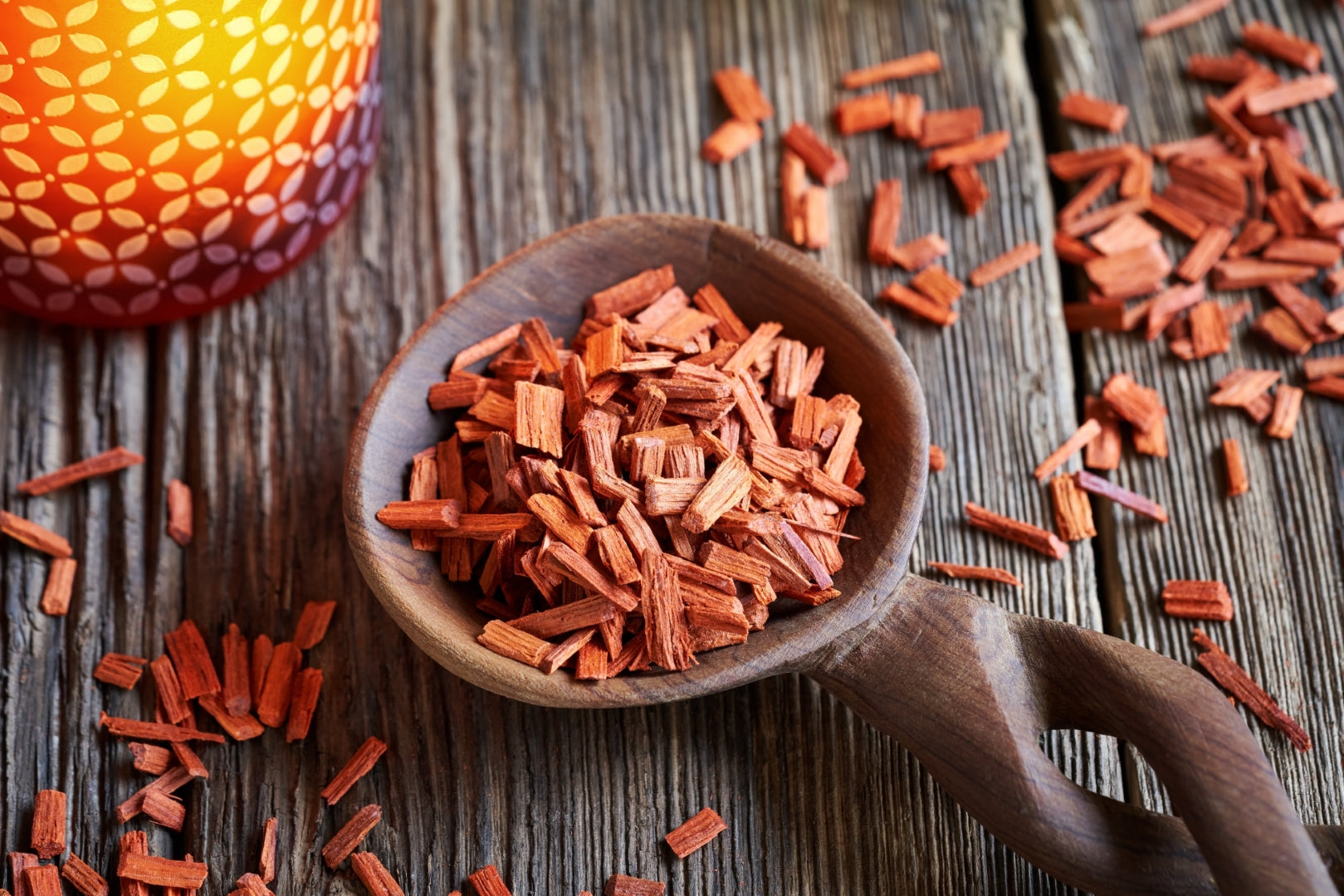 A few red woods chips in a wooden bowl on a wooden background.